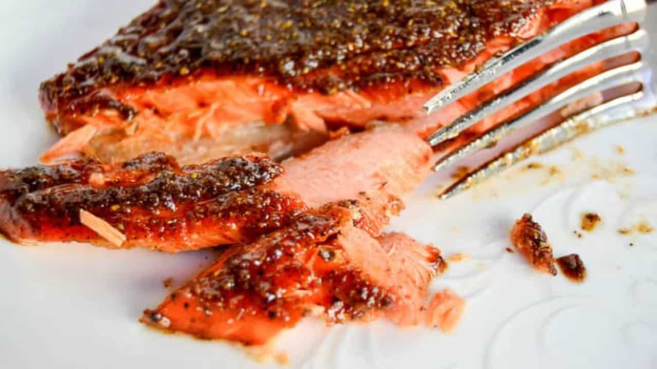 Cooked salmon fillet with a dark seasoning crust, partially flaked with a fork on a white plate.