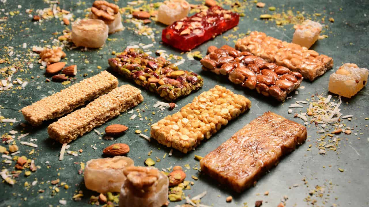 Assorted nut and sesame bars with scattered nuts and dried fruit on a green surface.