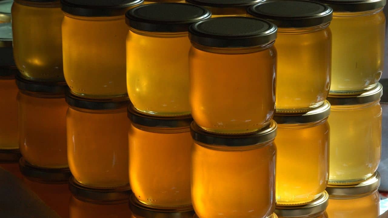Stacks of glass jars filled with golden honey, each sealed with a black lid, arranged in rows.