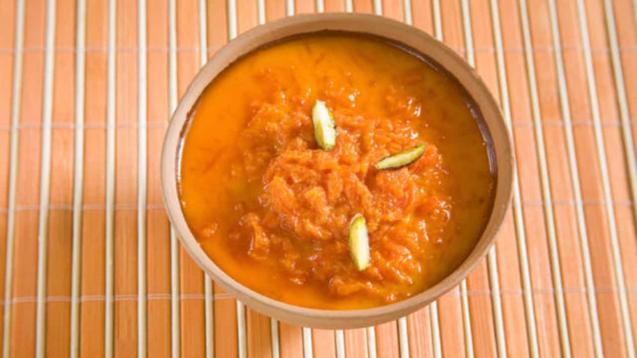 A bowl of orange dessert topped with sliced nuts, placed on a bamboo mat.