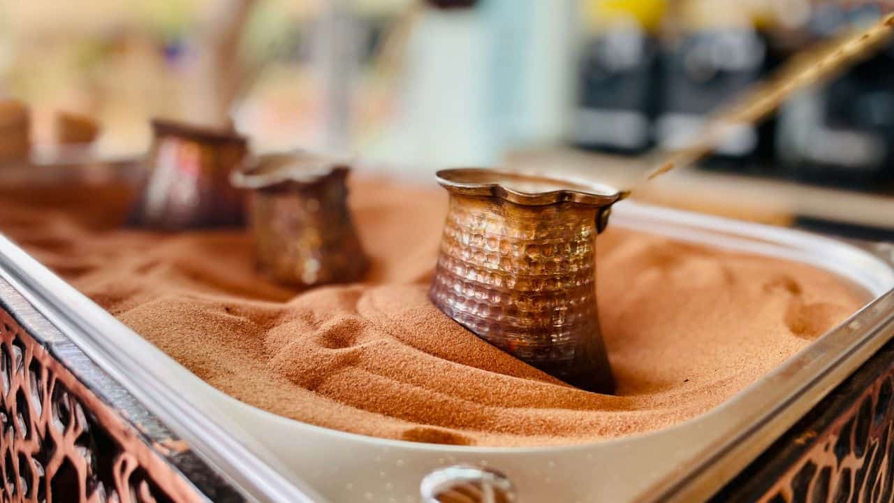Three copper cezves partially buried in fine sand, used for making traditional Turkish coffee.