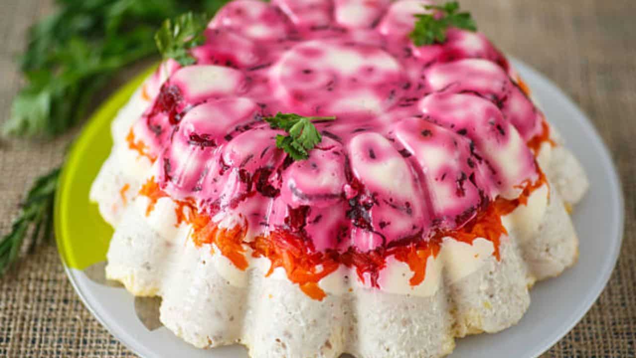 Layered salad with beetroot, carrots, and creamy dressing, garnished with parsley, presented on a white plate.