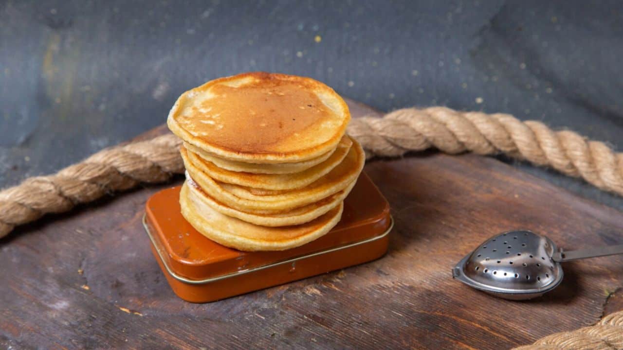A stack of pancakes on a rectangular tin with a rope and a metal tea infuser in the background.