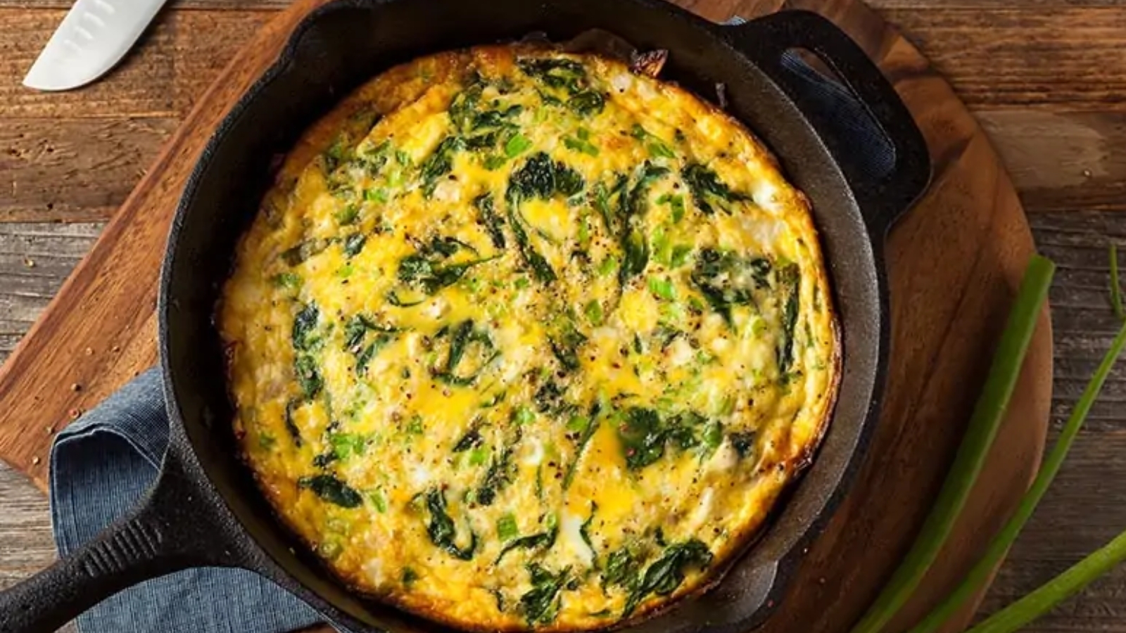 A spinach and cheese frittata in a black cast iron skillet on a wooden table.
