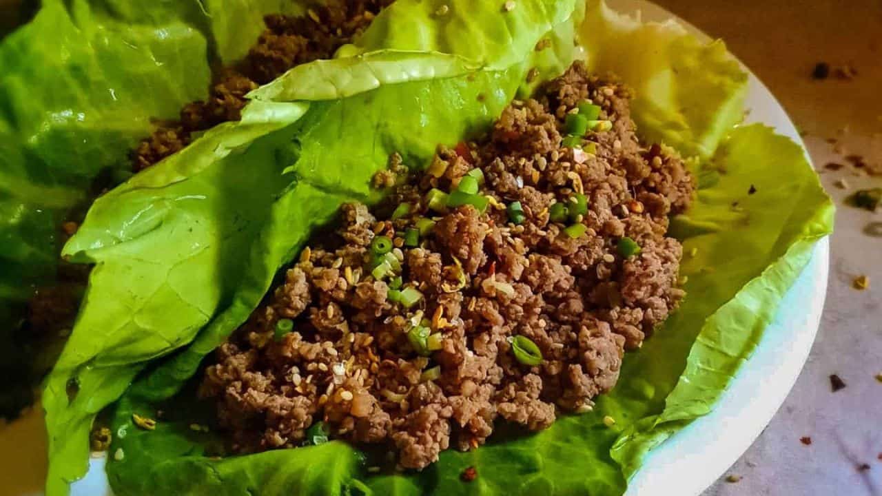 Ground meat seasoned with spices and chopped green onions, placed on large lettuce leaves on a white plate.