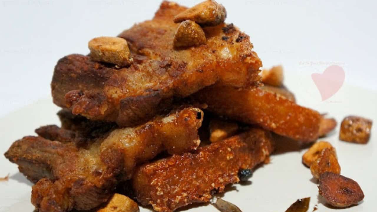 A stack of crispy fried pork belly pieces garnished with diced garlic on a white plate.