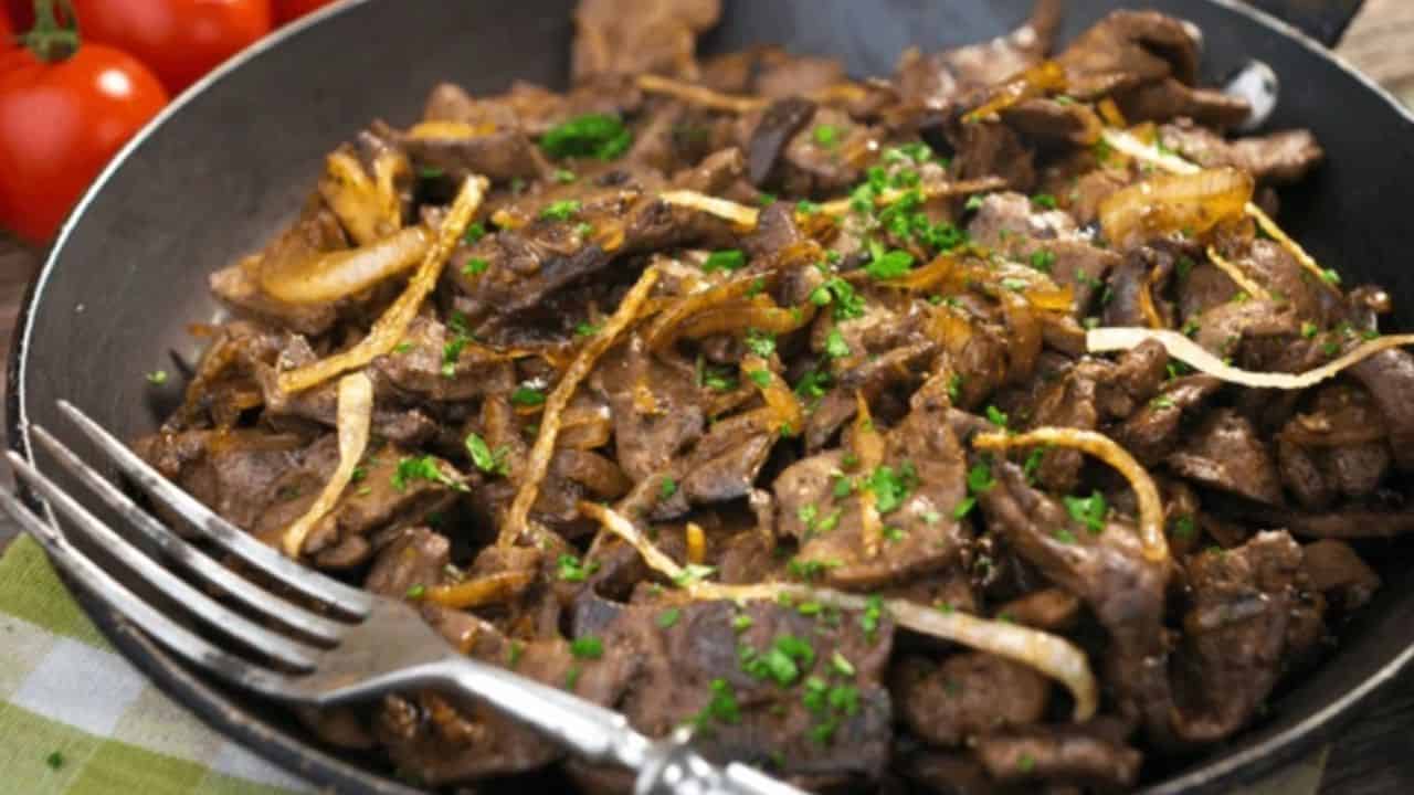 A skillet filled with cooked liver and onions, garnished with chopped parsley. A fork rests on the edge of the skillet.
