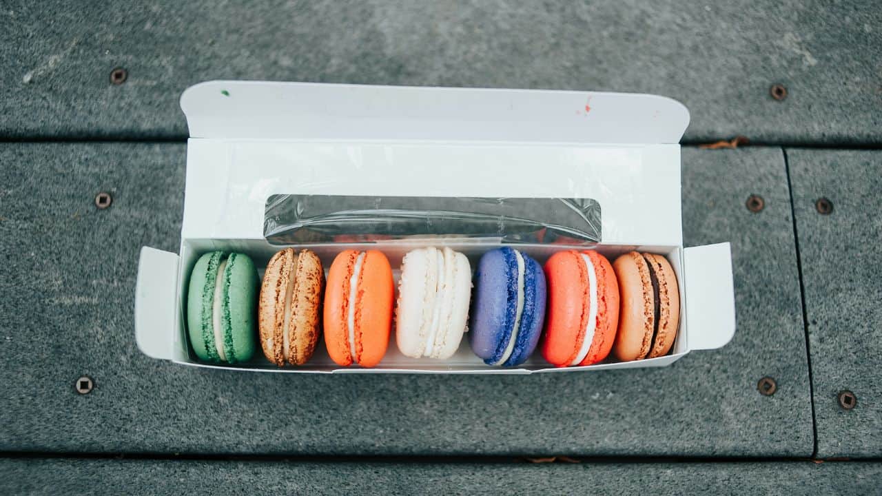 A box of seven colorful macarons placed on a wooden surface.