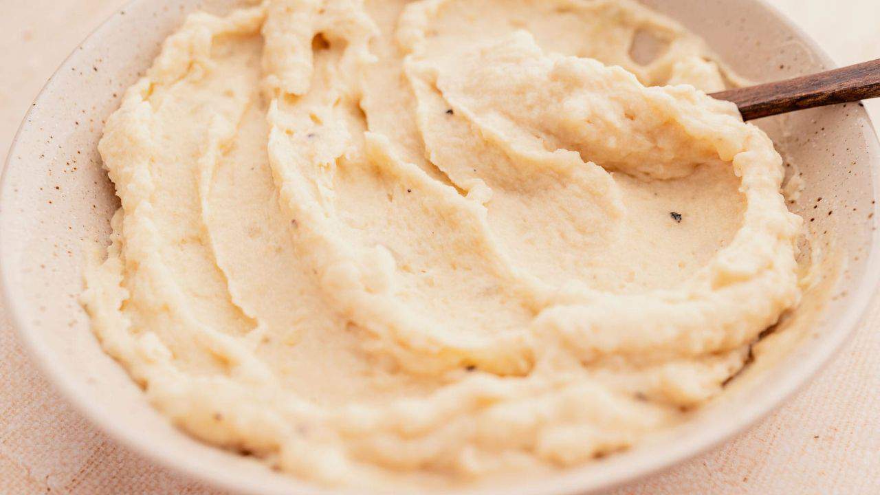 A bowl of creamy mashed potatoes with a wooden spoon.