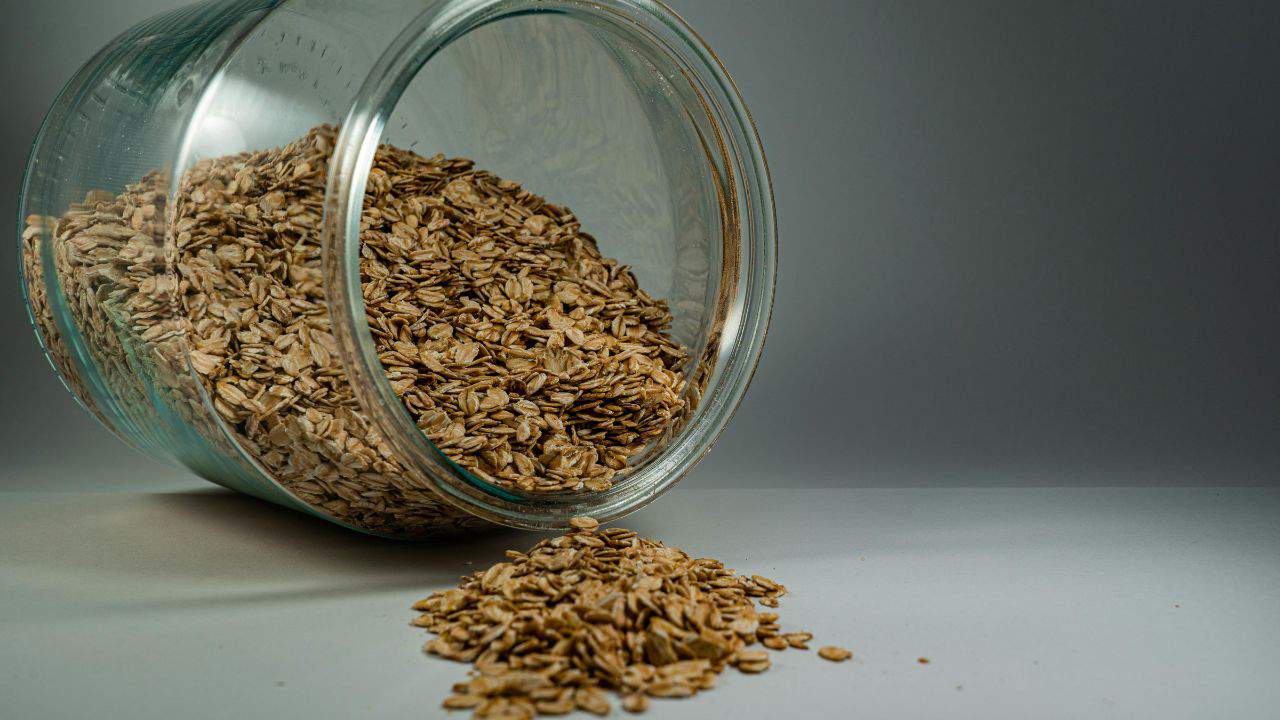A glass jar tipped over with oats spilling onto a surface.