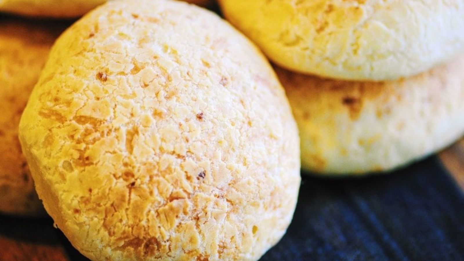 Close-up of a stack of golden, round cheese bread on a dark surface.