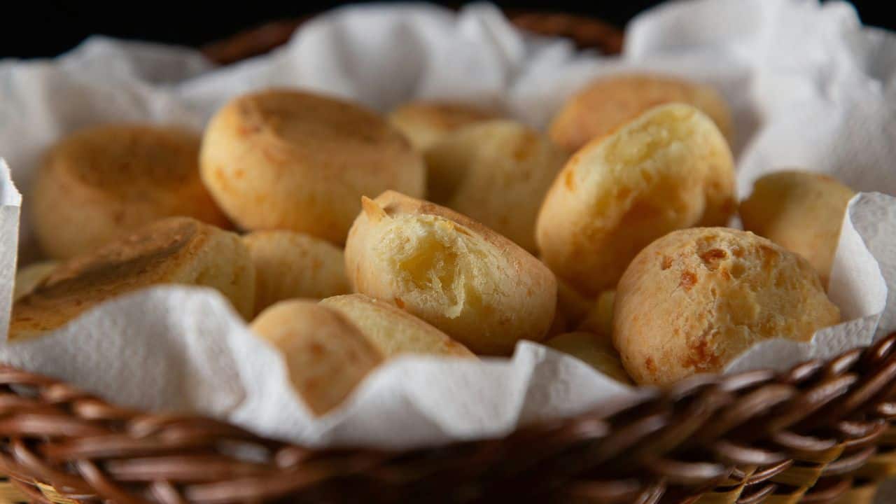 A basket filled with freshly baked, golden-brown cheese rolls on a white paper towel.