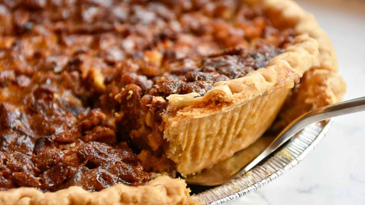 A close-up of a pecan pie with a slice being lifted out using a pie server.