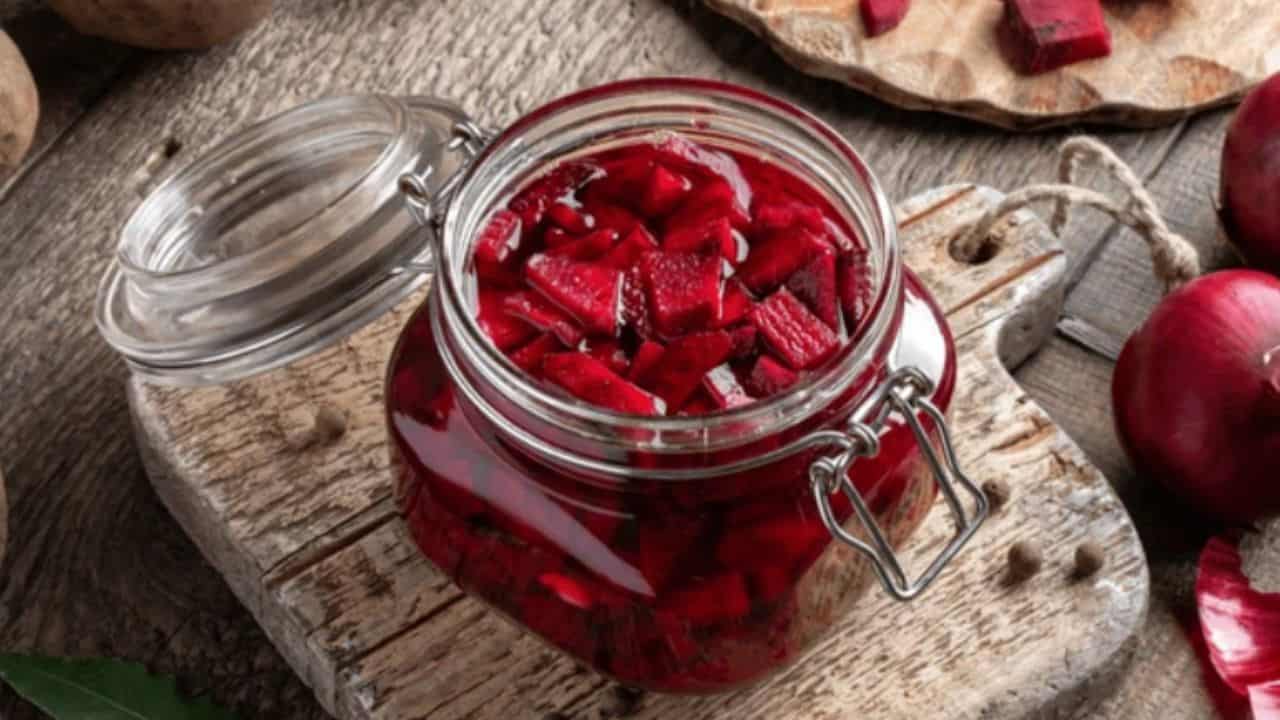 A glass jar filled with chopped pickled beets sits open on a rustic wooden board.