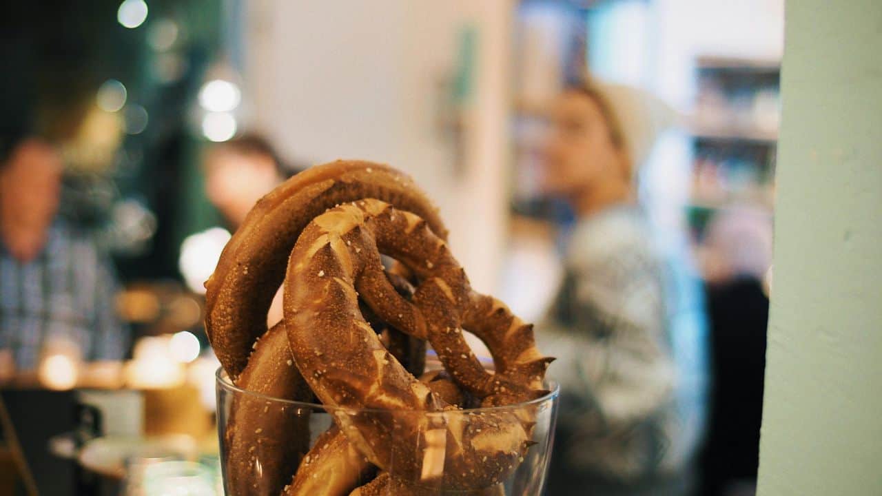 Close-up of pretzels in a clear glass container in a cozy café setting, with blurred people in the background.