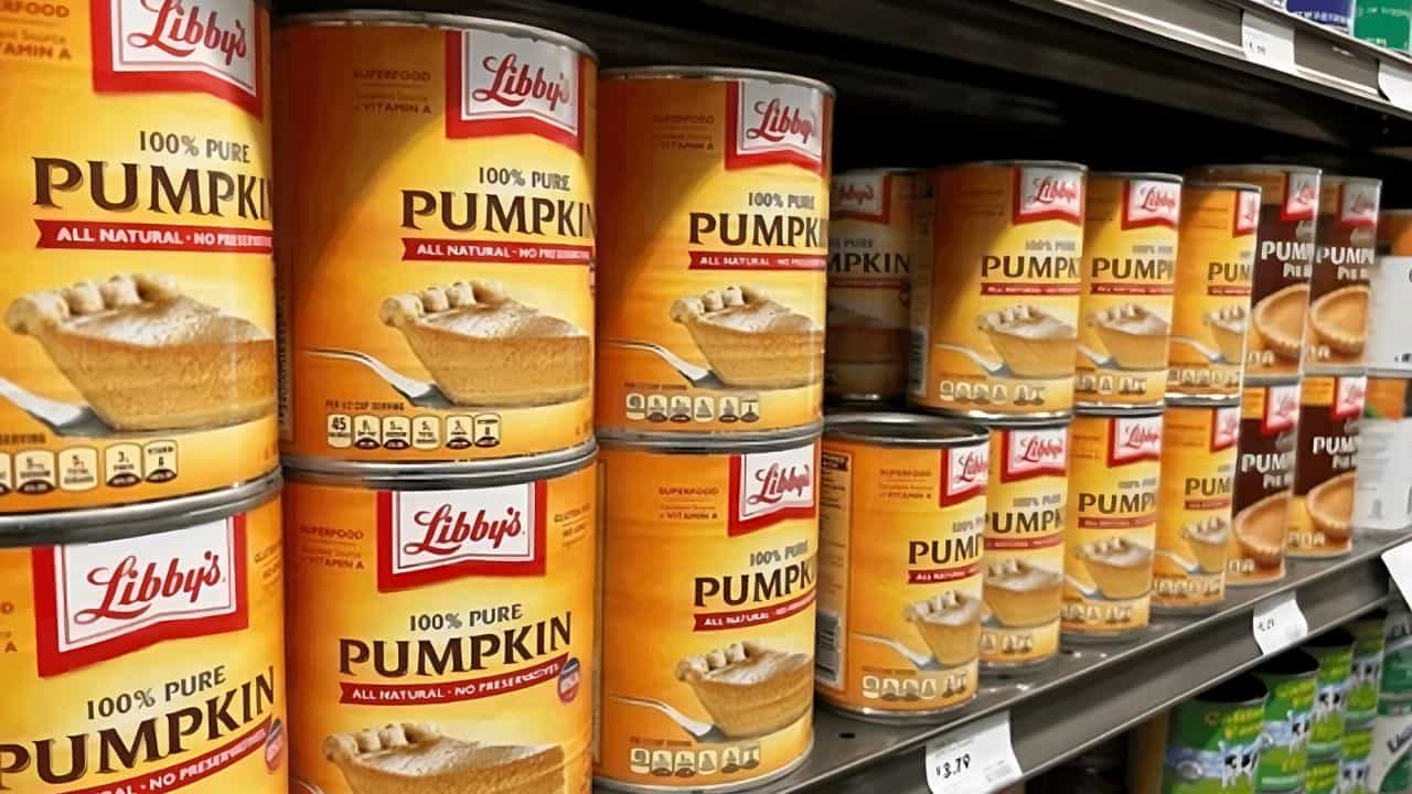 Cans of Libby's 100% Pure Pumpkin are lined up on a grocery store shelf, each displaying a label depicting a pumpkin pie.