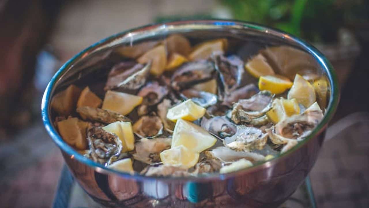 A bowl filled with raw oysters and lemon wedges.