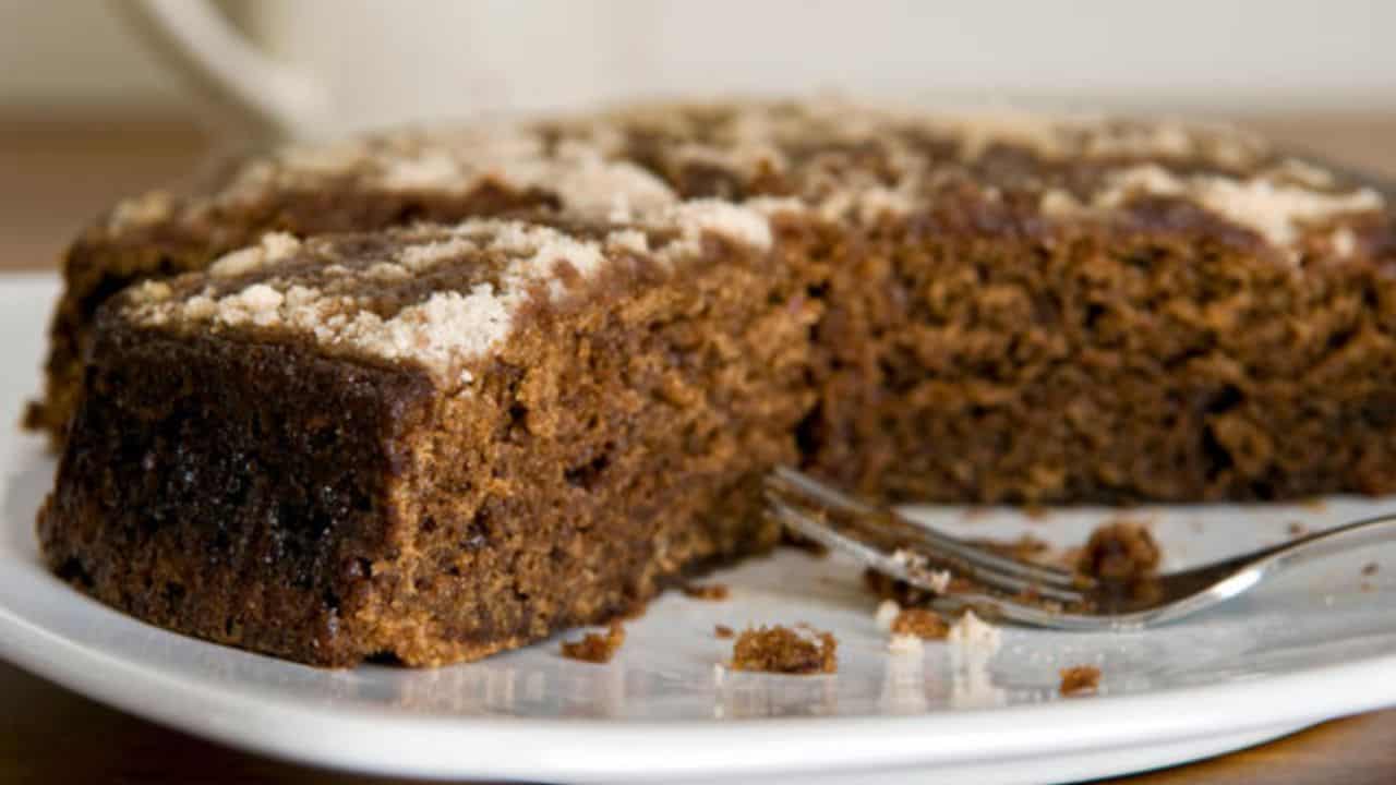 A round, sliced gingerbread cake on a white plate with a fork beside it. The cake has a crumbly topping.