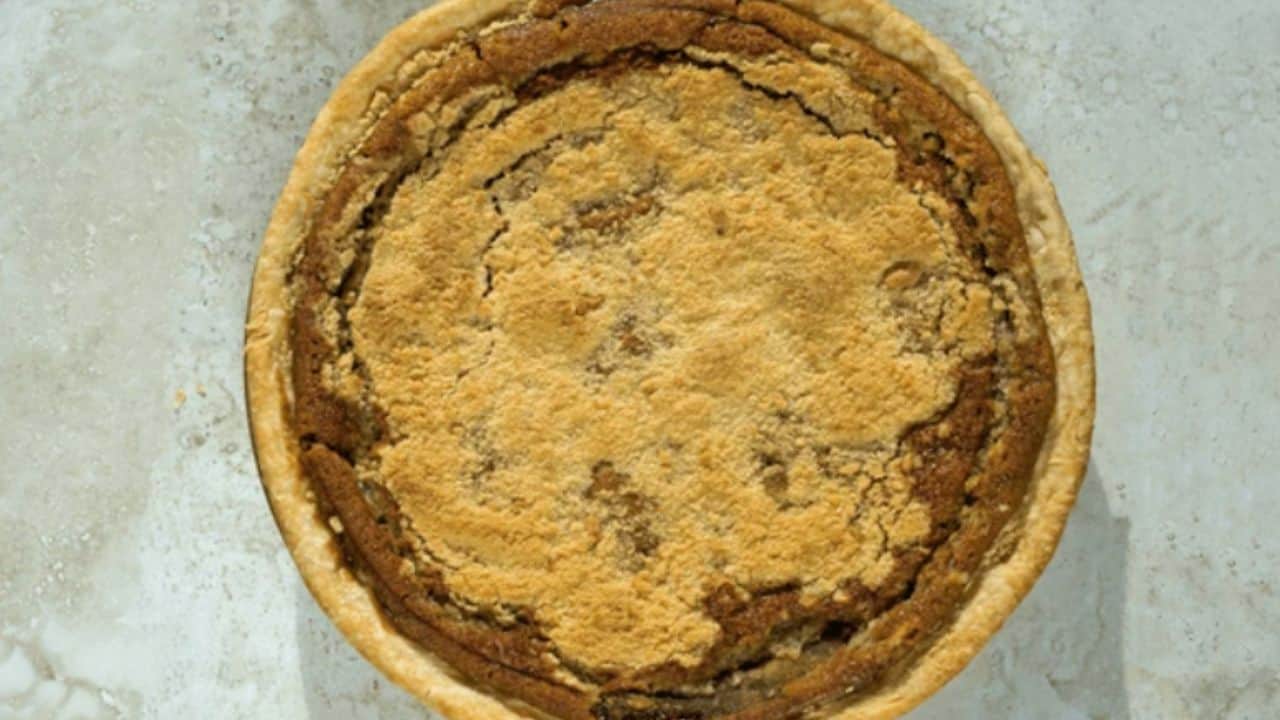 A whole brown pie with a crumbly crust on a light-colored surface.