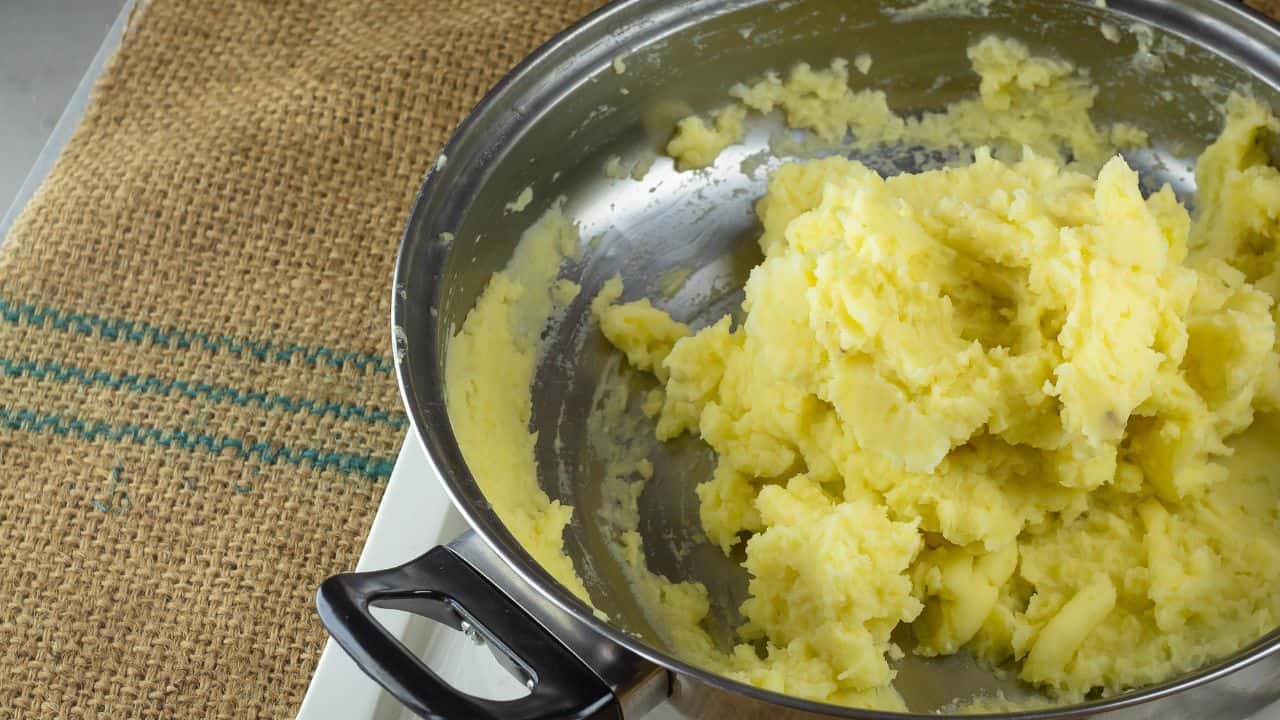 Mashed potatoes in a stainless steel pot on a burlap-covered table.
