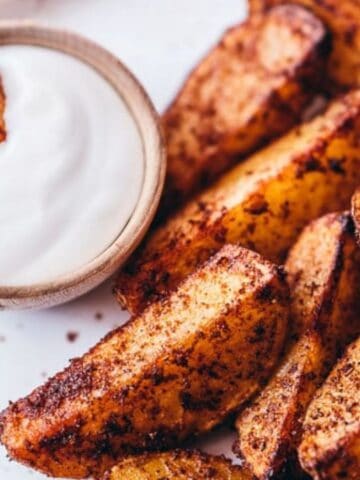 A plate of seasoned potato wedges with a small bowl of white dipping sauce.