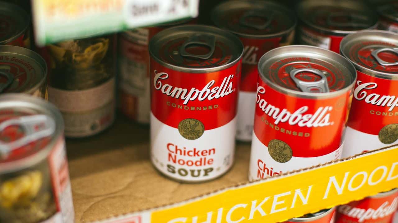 Cans of Campbell's Chicken Noodle Soup are displayed on a store shelf in a cardboard box.