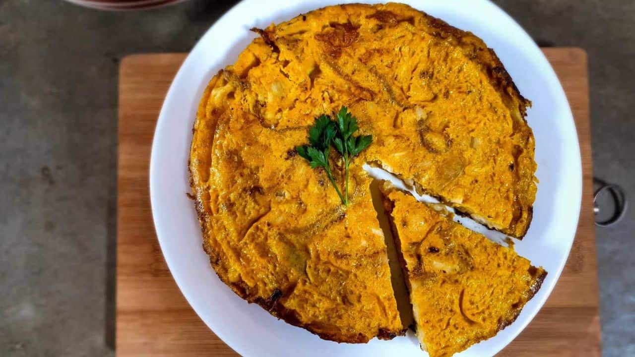 A round omelette with one slice cut out, garnished with parsley on top, served on a white plate.