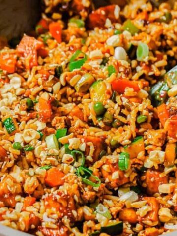 A skillet filled with mixed fried rice, including diced vegetables and pieces of meat, stirred with a spatula.