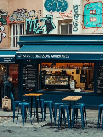 Street scene showing people outside a café with blue stools, surrounded by graffiti on building walls.