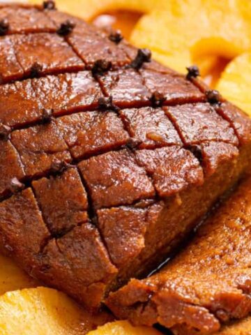 A glazed ham with a diamond pattern is surrounded by pineapple slices.