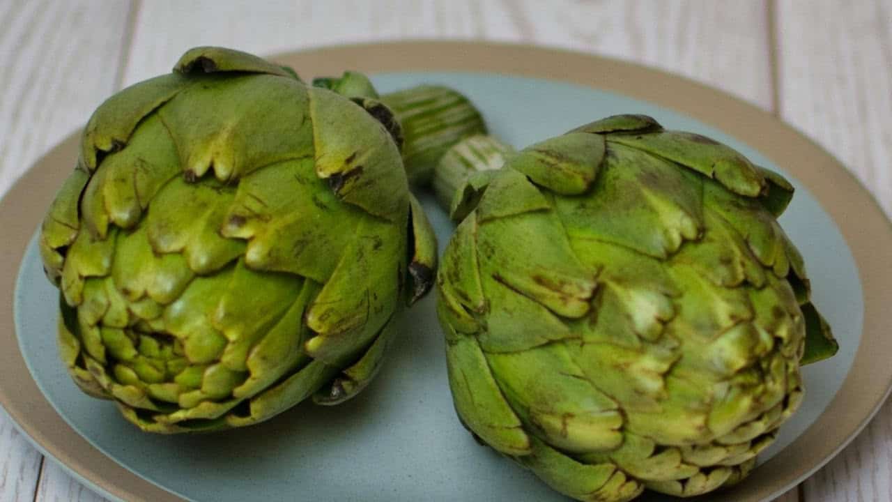 Two fresh artichokes on a round plate with a wooden background.