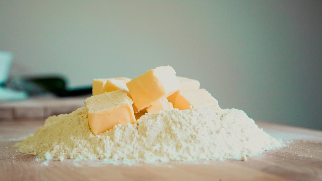 Cubes of butter placed on a mound of flour on a wooden surface.