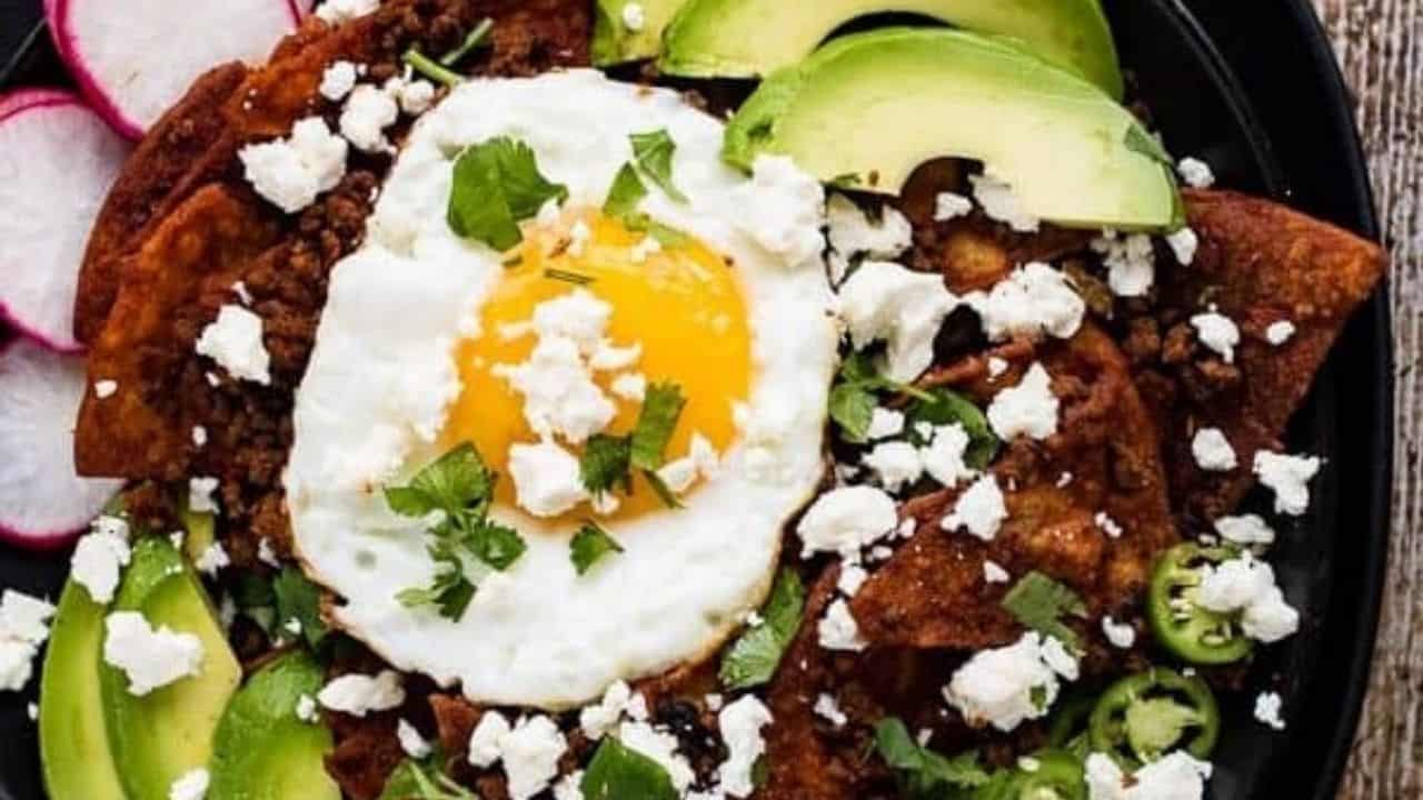 Overhead shot of chilaquiles on a black plate with a fork and knife on the side.