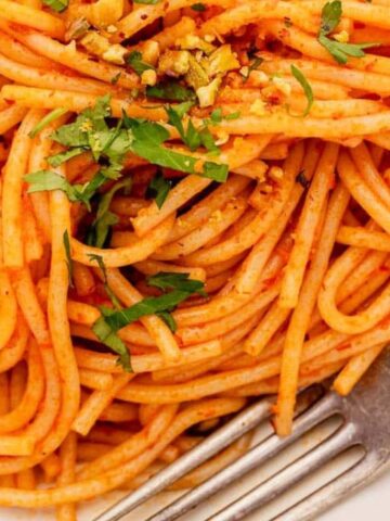 Plate of spaghetti topped with herbs and spices, accompanied by a fork.