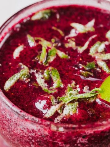 A glass of vibrant red juice garnished with mint shreds and a lime wedge.