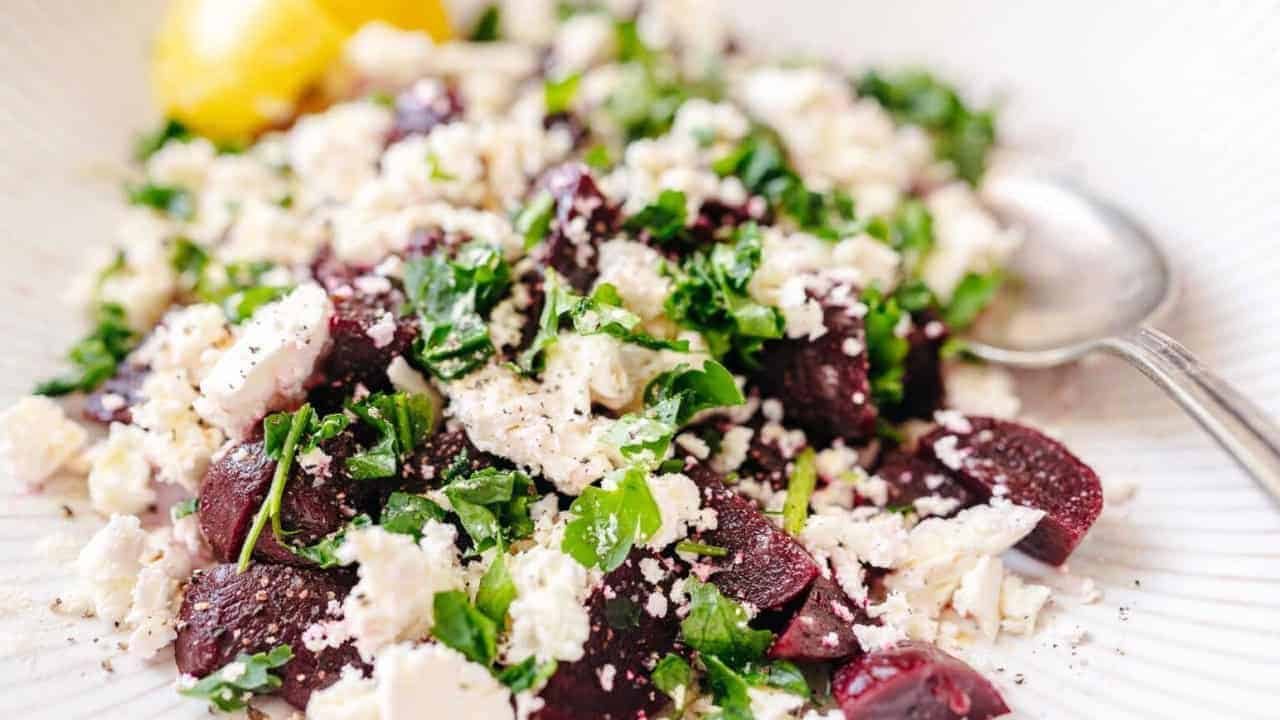 A salad with chopped beets, crumbled cheese, fresh parsley, and a spoon, garnished with lemon.