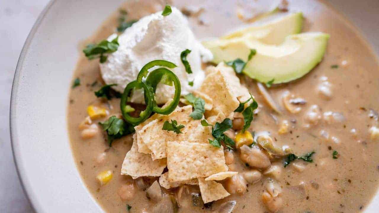 A bowl of creamy soup topped with tortilla chips, sliced jalapeños, cilantro, sour cream, and avocado slices.