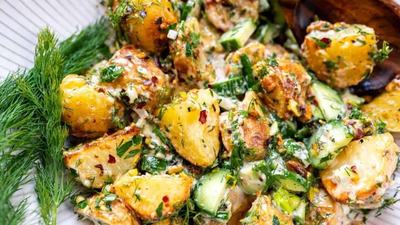 Close-up of a potato salad with dill, cucumber, herbs, and a creamy dressing.