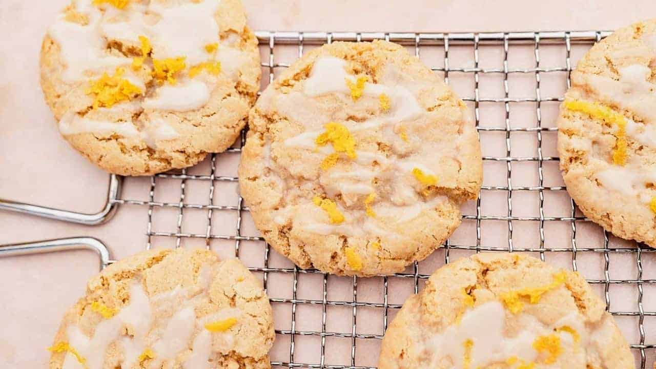 Five lemon cookies with icing and lemon zest on a cooling rack.