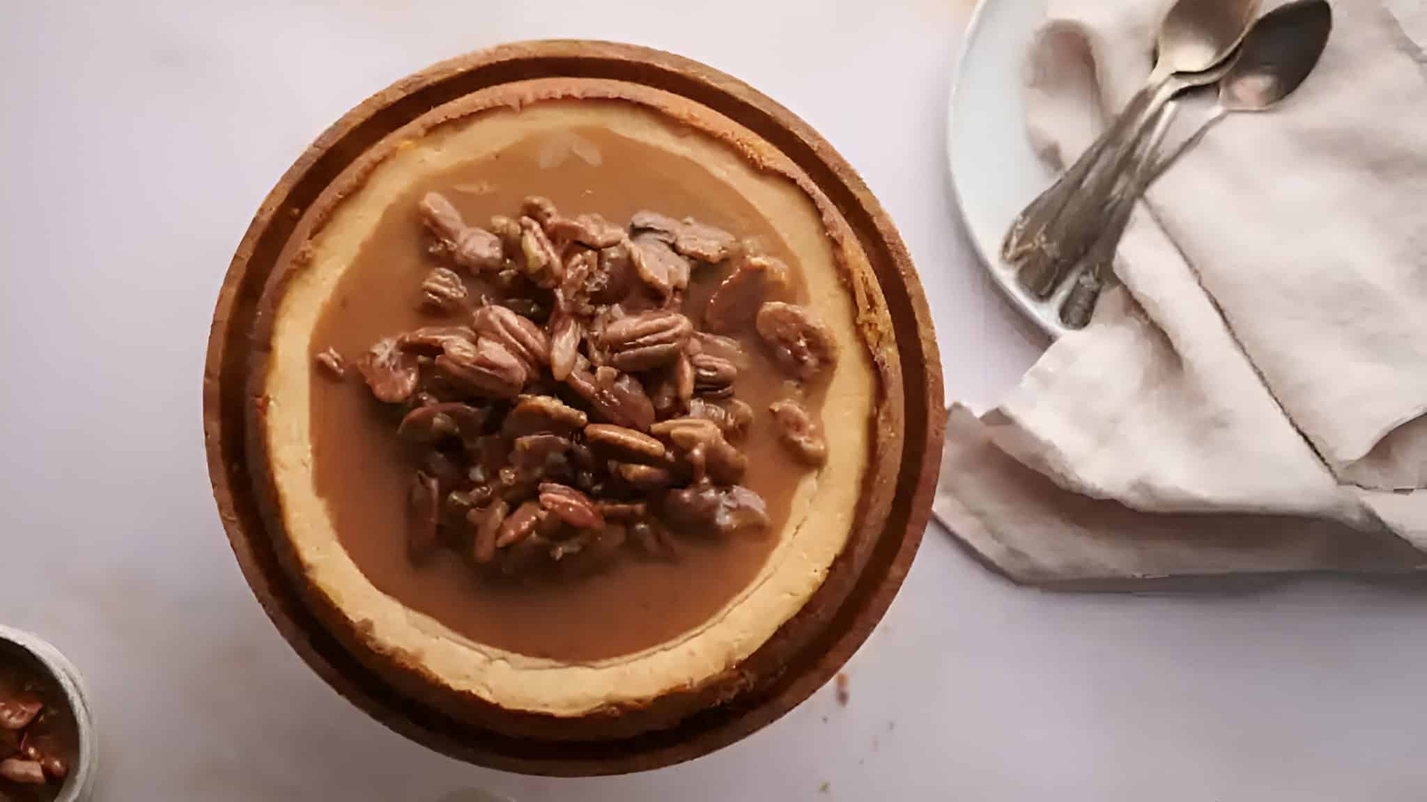 A pie topped with pecans on a table next to a plate with spoons and a napkin.