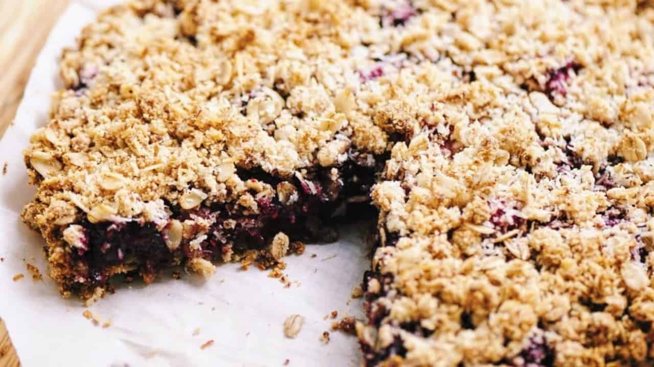 A close-up of a baked crumble pie with a missing slice, showcasing a golden oat topping covering a berry filling, resting on parchment paper.