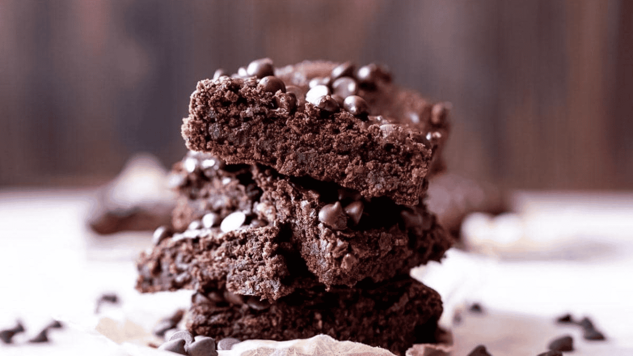 A stack of chocolate brownies with chocolate chips, placed on parchment paper.