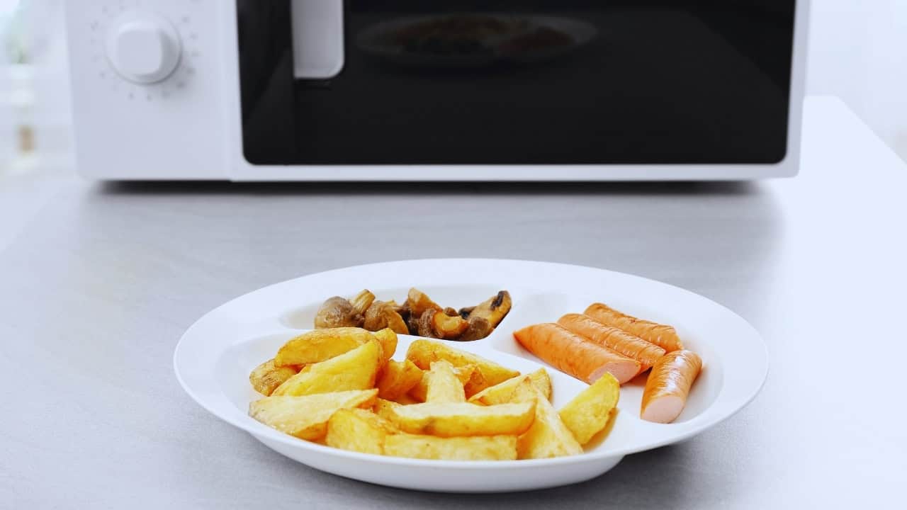 A plate with potato wedges, sautéed mushrooms, and carrot sticks on a countertop in front of a microwave.