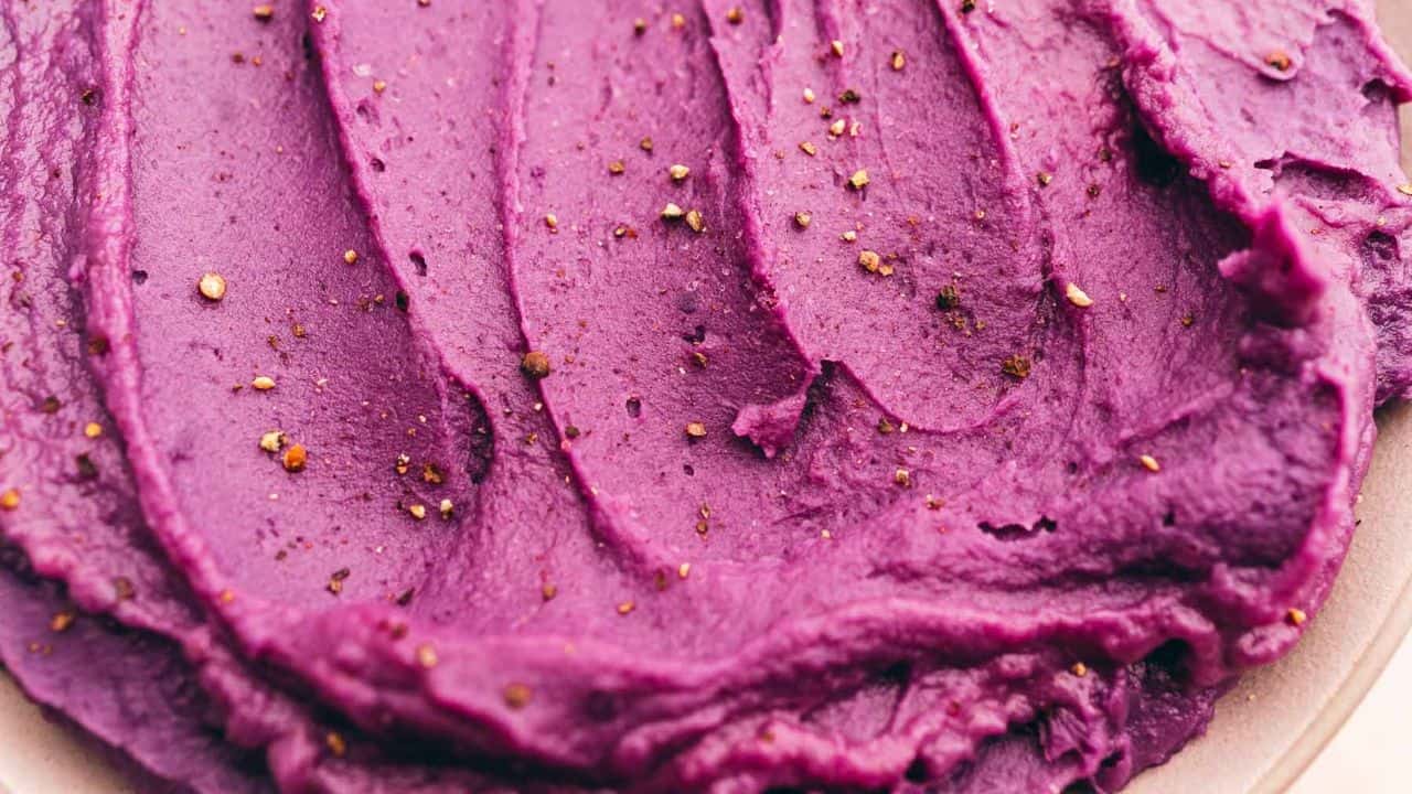 Close-up of creamy purple mashed potatoes with pepper flakes sprinkled on top.