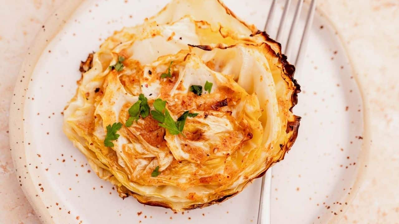 Grilled cabbage slice garnished with parsley on a white plate with a fork.