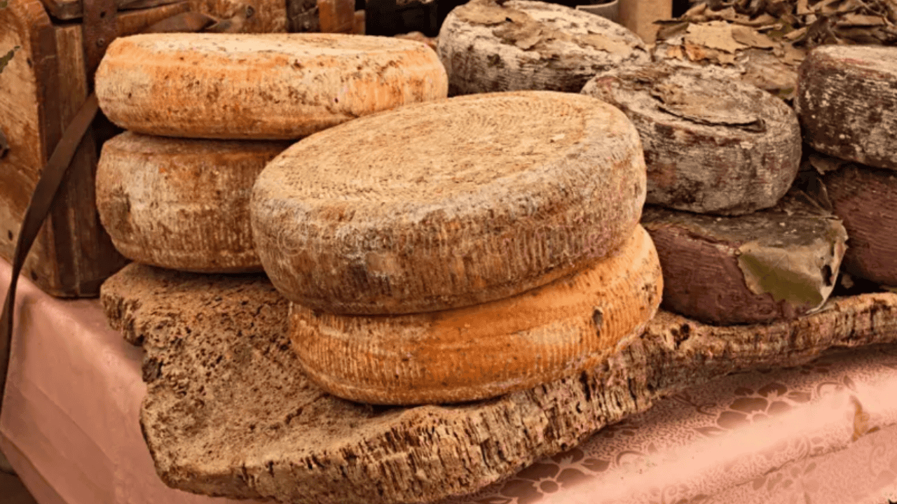Several large, round cheese wheels stacked on a wooden surface, displayed at a market stall.