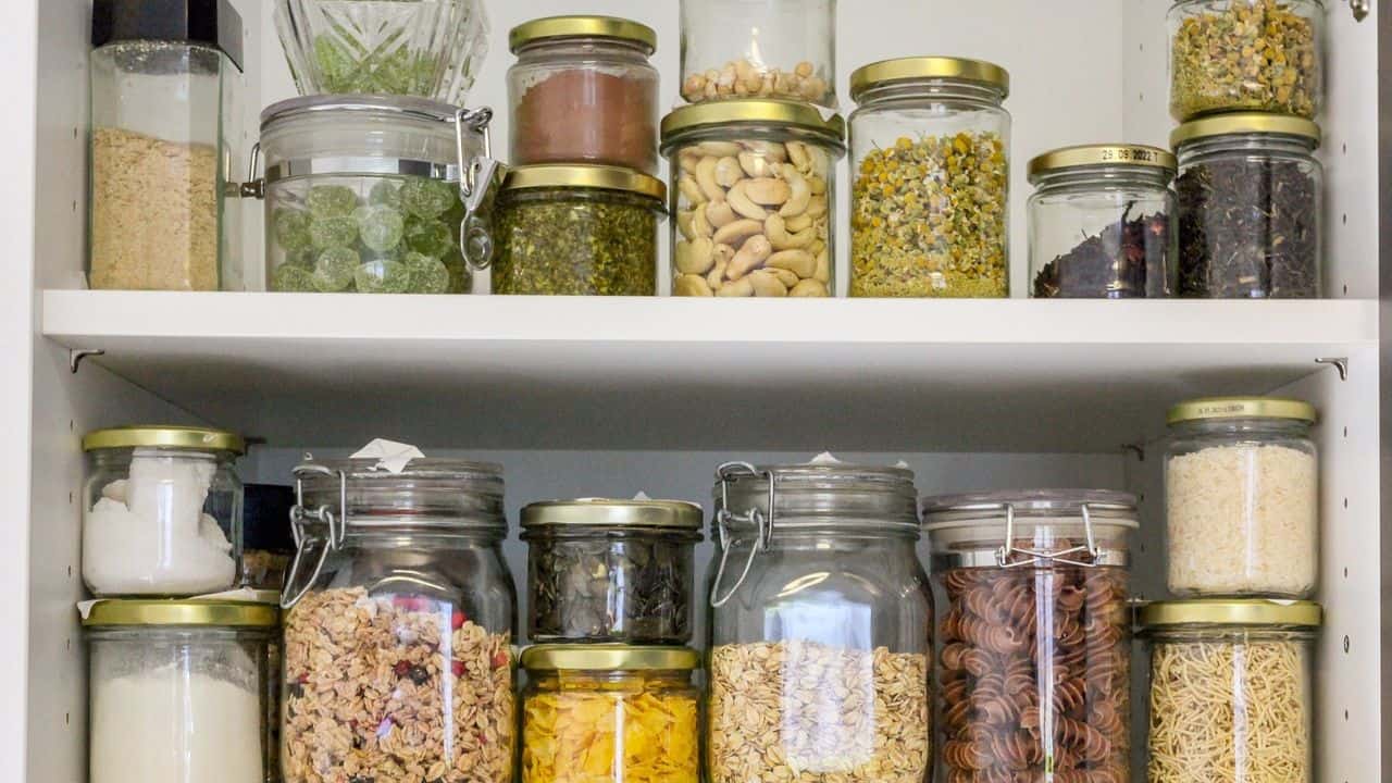 Pantry shelves with assorted glass jars filled with various dried ingredients, including pasta, grains, nuts, and spices.