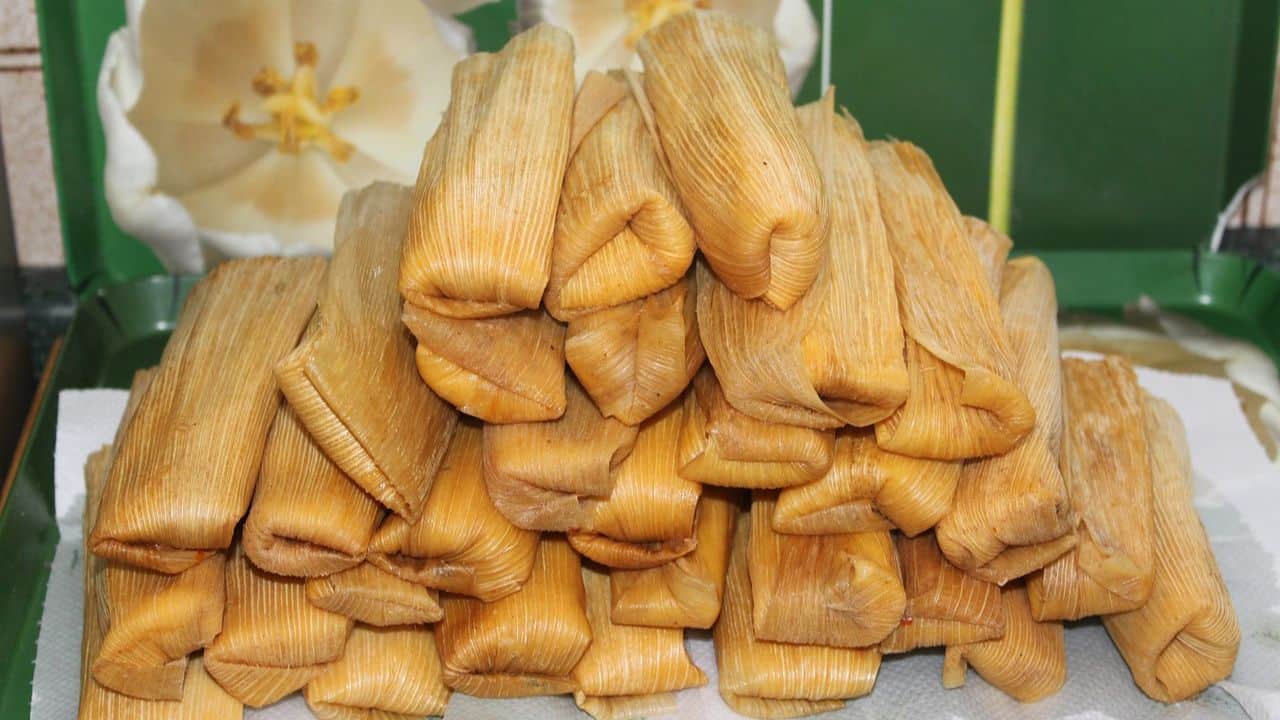 A stack of tamales wrapped in corn husks, placed on a green surface with a paper towel underneath.