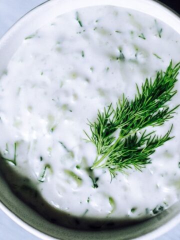 Bowl of creamy white tzatziki garnished with fresh dill on top.