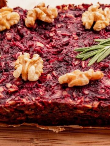 A rectangular beet and nut loaf garnished with walnuts and rosemary sprigs, displayed on a wooden surface.